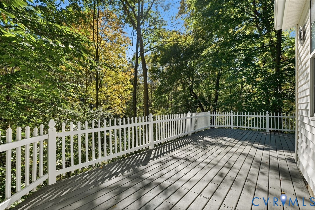 Elevated deck featuring gray composite decking and a white picket-style railing, surrounded by mature trees