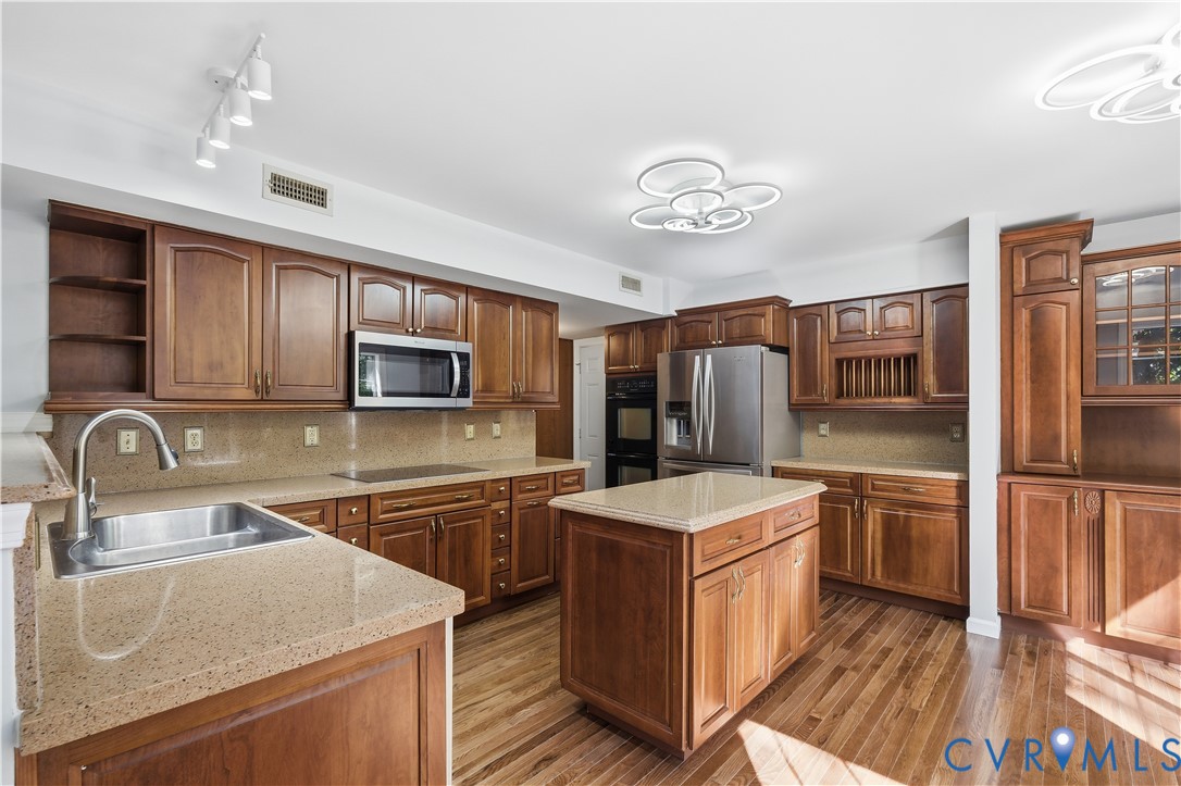 Kitchen featuring stained wood cabinetry, stone countertops, a central island, stainless steel appliances, and wood-finish flooring
