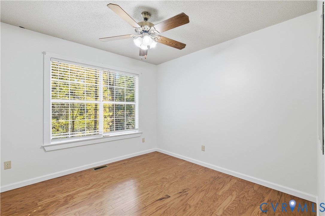 Interior room featuring wood-finish flooring, a multi-pane window, and a ceiling fan with integrated lighting