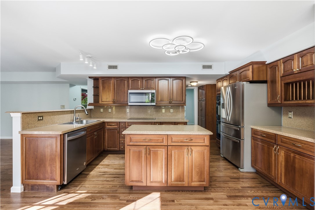 Kitchen featuring stained wood cabinetry, stone-finish countertops, stainless steel appliances, central island, and wood-finish flooring