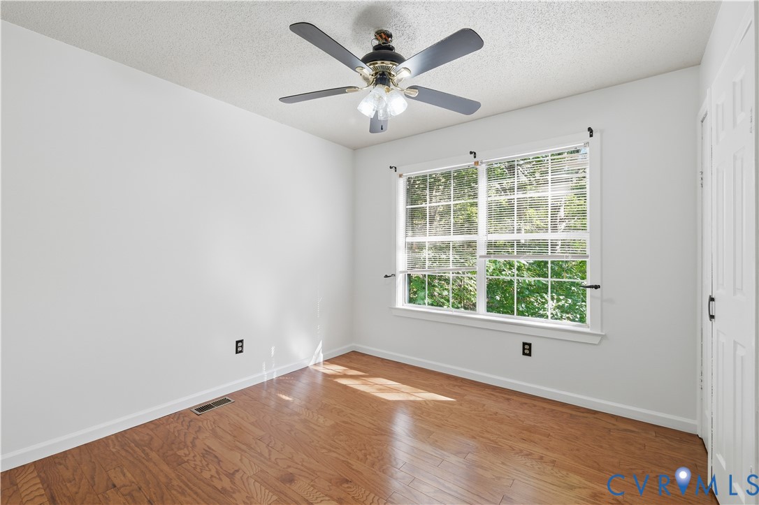 Wood-finish flooring, multi-pane window with blinds, ceiling fan with integrated light fixture, and six-panel interior door