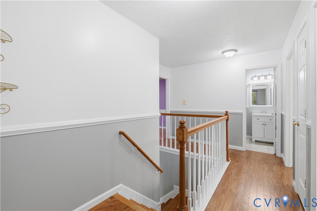 Hallway featuring wood-finish flooring, white railings with a wooden handrail, chair rail molding, and flush-mount ceiling lighting
