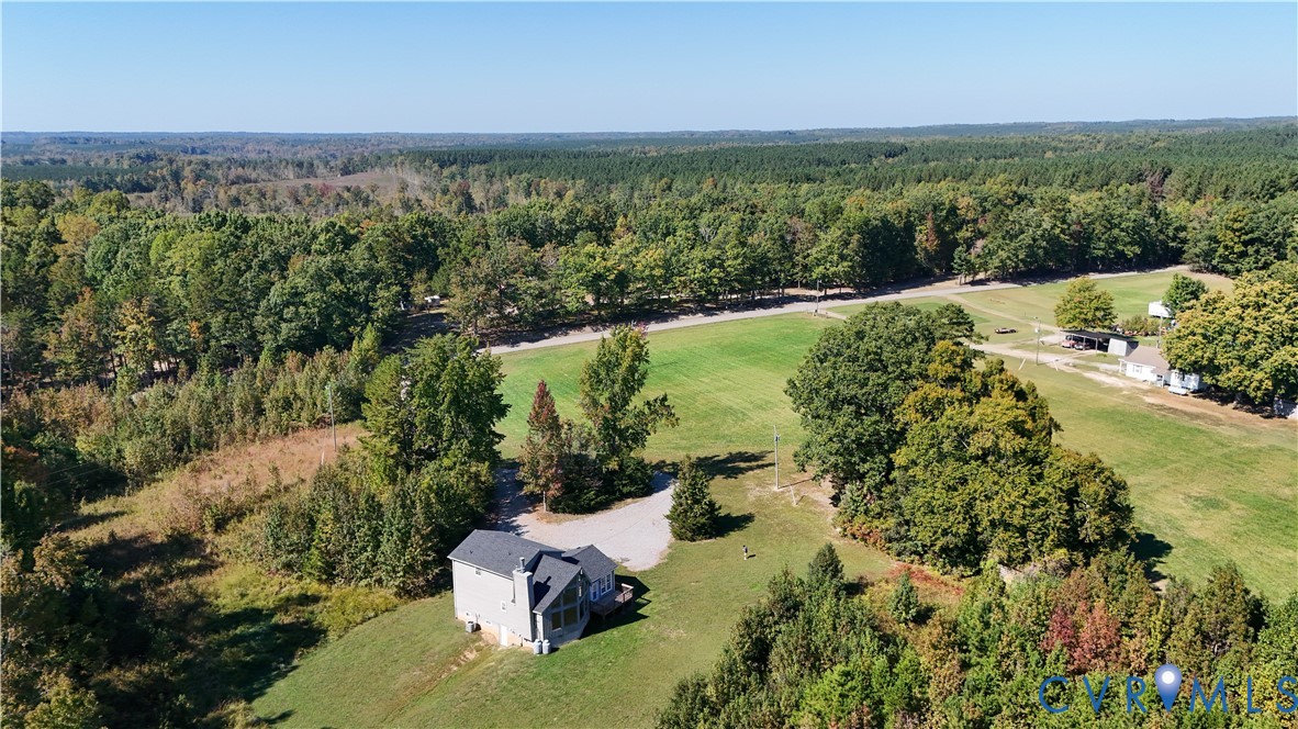 Aerial perspective of a multi-story residence situated on a large lot featuring extensive acreage, mature perimeter trees, and an open grass field