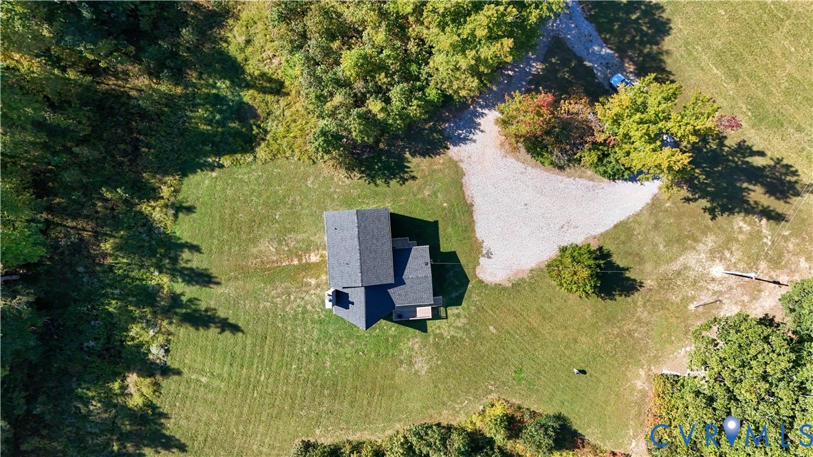 Aerial perspective featuring a shingled roof structure, a sprawling grass yard, mature perimeter trees, and a gravel driveway