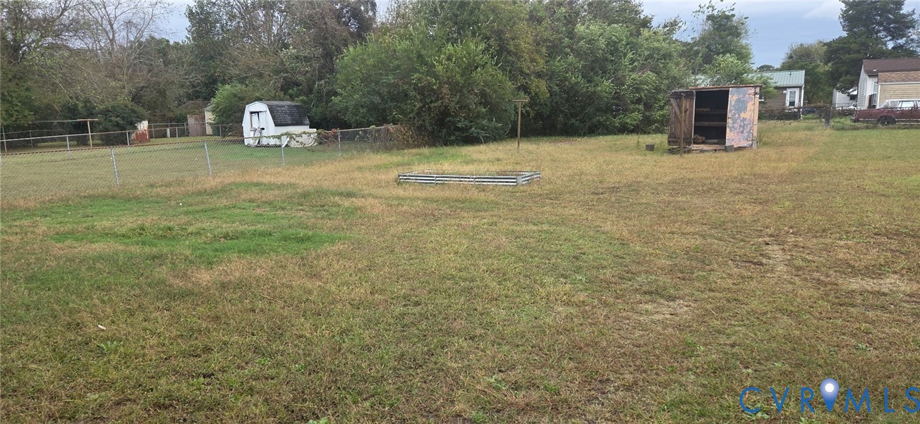 Expansive level lot featuring mature trees, chain-link perimeter fencing, and dual detached storage structures