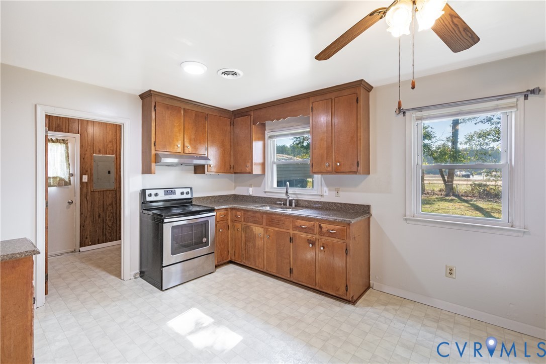 Kitchen featuring wood cabinetry, stone-finish countertops, stainless steel range with overhead hood, and a ceiling-mounted fan