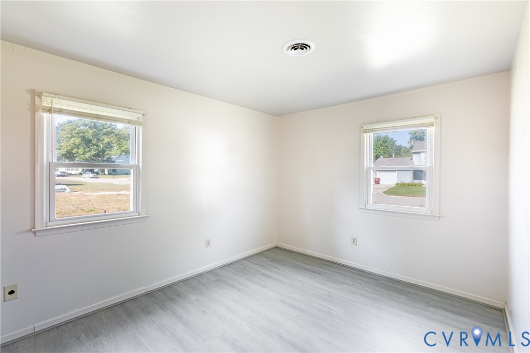 Neutral-toned interior room featuring wood-finish flooring, dual windows with white horizontal blinds, and smooth-finish walls