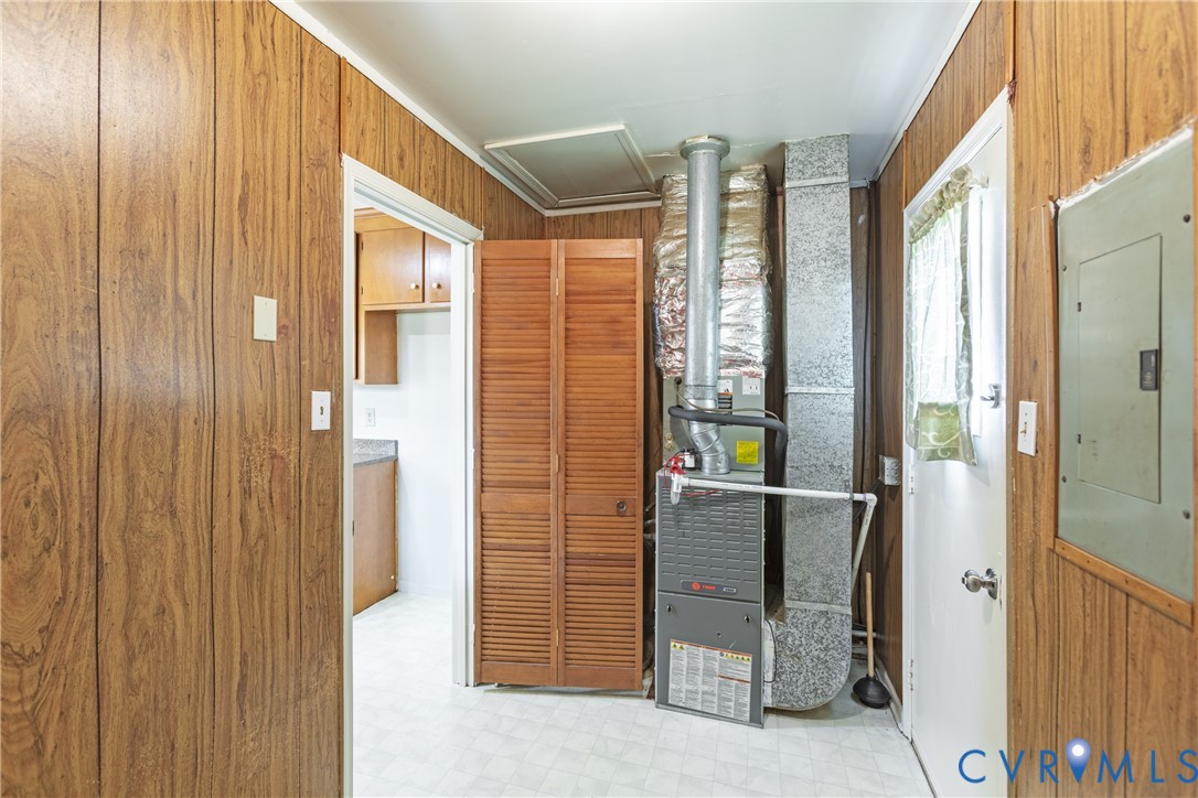 Utility room featuring wood-finish paneling, louvered wood closet doors, and a forced-air furnace unit