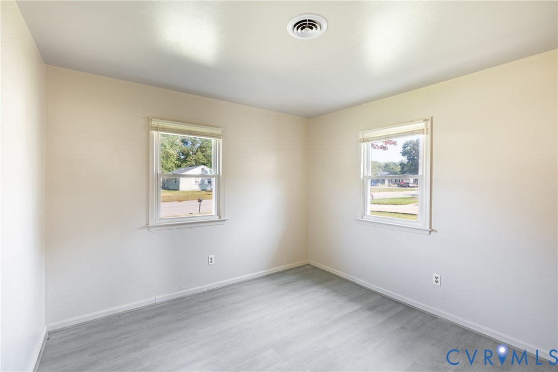 Neutral-toned interior space featuring light wood-finish flooring, two double-hung windows with white casing, and white walls