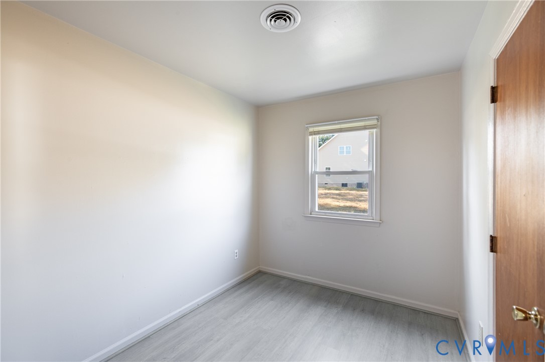 Interior room featuring neutral-toned walls, wood-finish flooring, and a single window with white trim