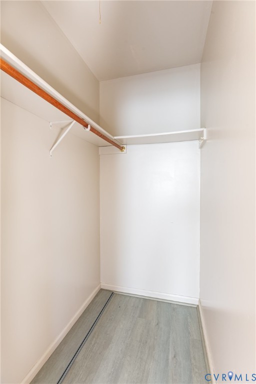 Walk-in closet featuring wood-finish flooring, white shelving, and a mounted hanging rod