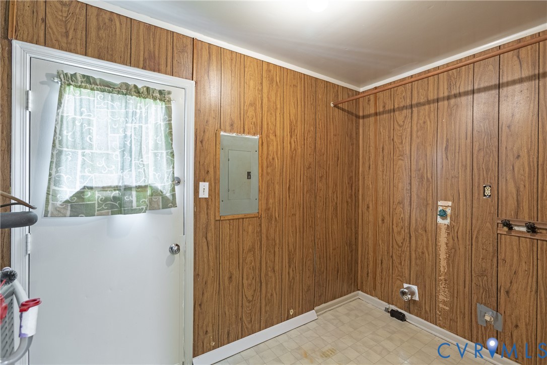 Utility area featuring wood-paneled walls, vinyl flooring, an integrated electrical service panel, and built-in wall-mounted hanging rod