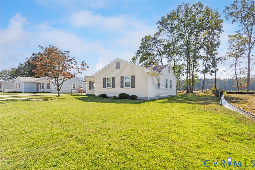 Single-story residence with light-colored horizontal siding, dark decorative window shutters, and a gable roofline situated on a sprawling parcel featuring expansive grass lawn and mature perimeter trees