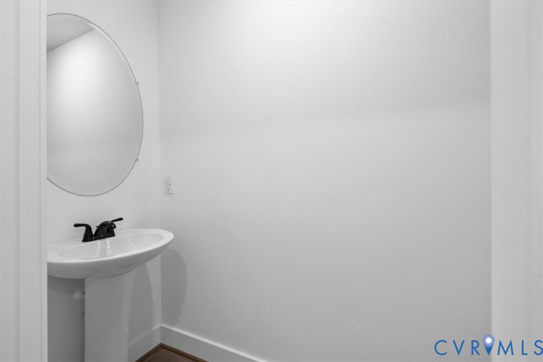 Pedestal sink featuring a white basin and matte black faucet, paired with a frameless oval wall-mounted mirror