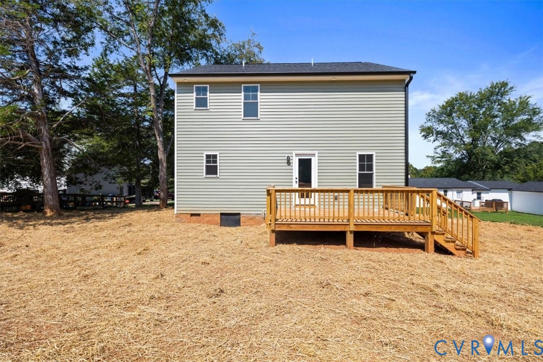 Two-story exterior featuring light-colored horizontal siding, a dark shingle roof, and a raised wooden deck with railings and staircase