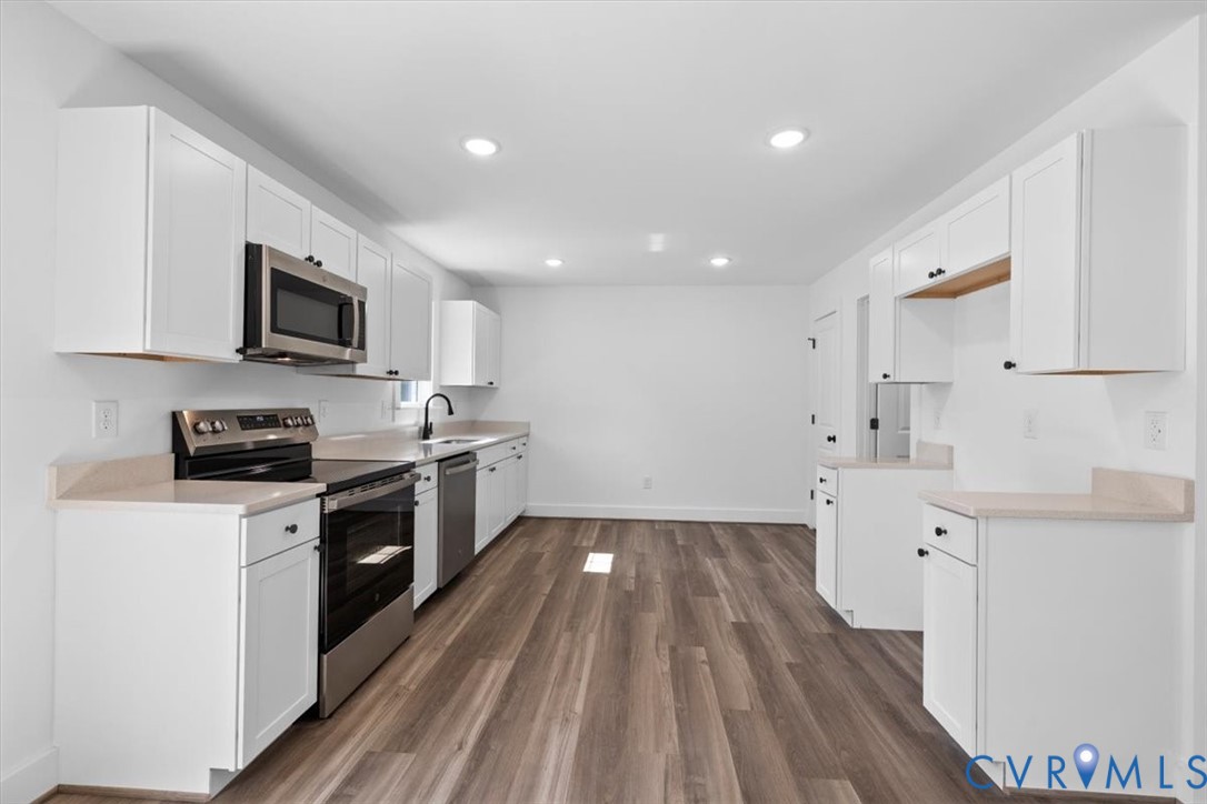 Kitchen featuring white cabinetry, solid-surface countertops, stainless steel appliances, and wood-finish flooring