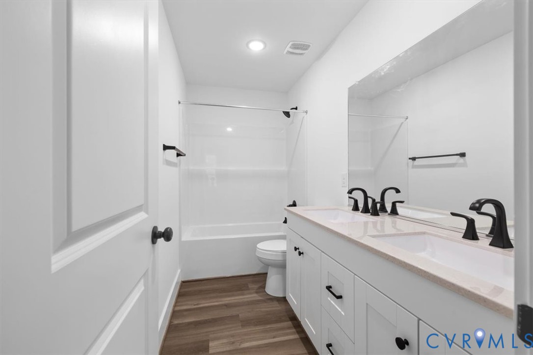 Dual-sink vanity with a light-toned countertop, matte black fixtures, wood-finish flooring, and a full-width mirror