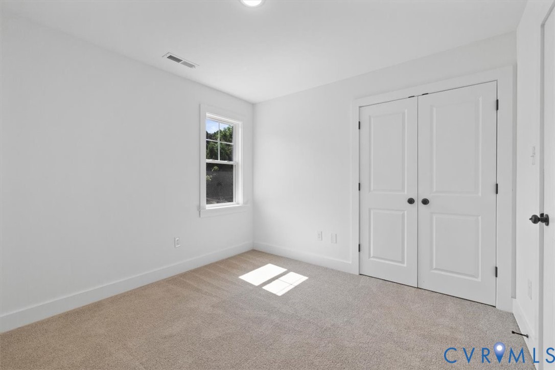 Neutral-toned carpeting, double-panel closet doors with matte black hardware, single-hung window with muntin detailing, and clean white interior wall finish
