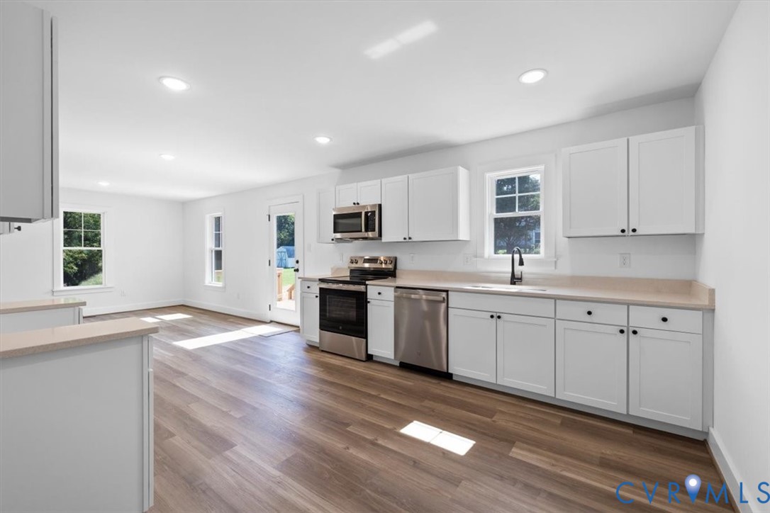 Kitchen featuring white shaker-style cabinetry, stainless steel appliances, solid-surface countertops, recessed lighting, and wood-finish flooring