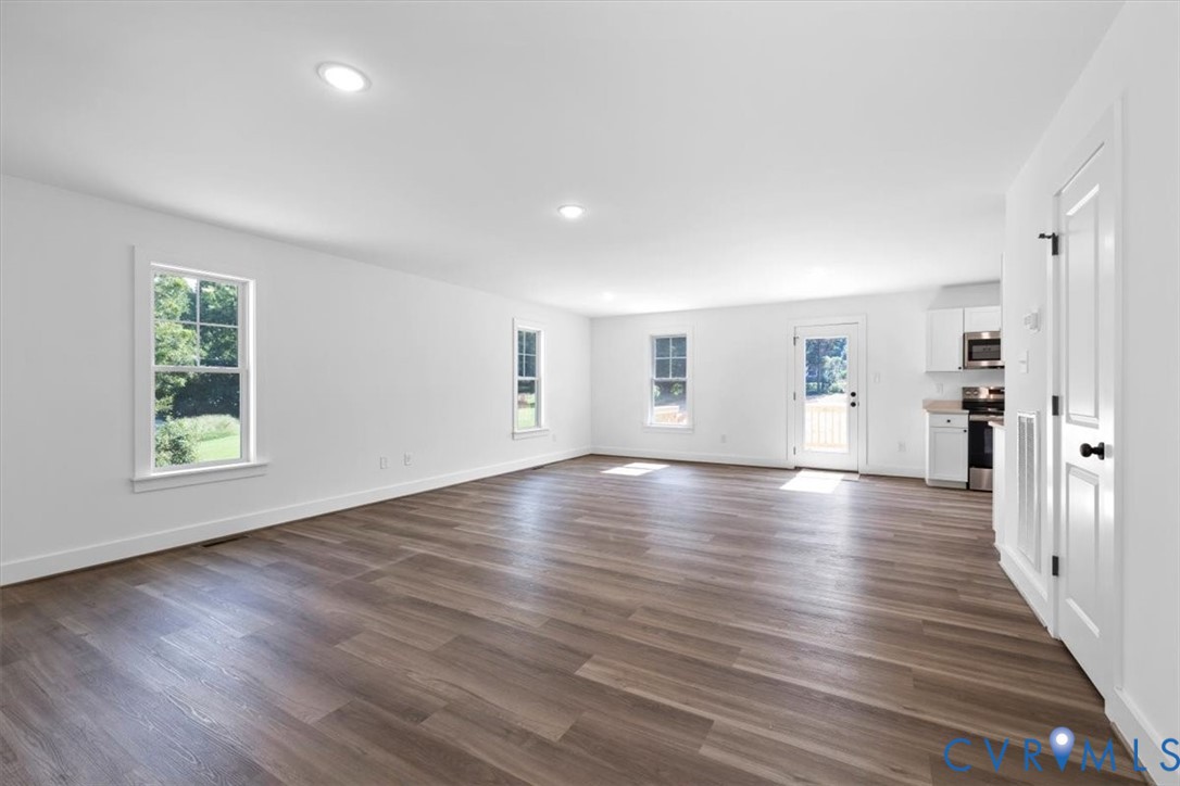 Open-concept interior featuring wood-finish flooring, recessed lighting, double-hung windows, and white shaker-style cabinetry with integrated stainless steel appliances