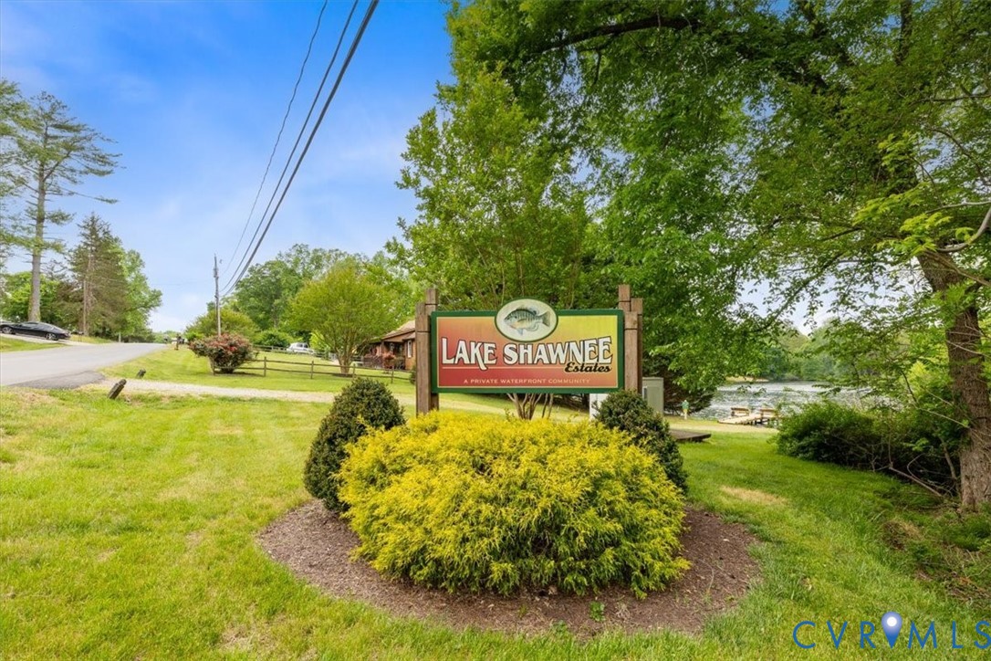 Community entrance sign featuring wooden posts and landscaped garden beds with evergreen shrubs