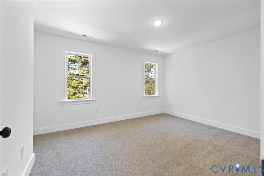 Neutral-toned carpeting, recessed ceiling lighting, and double-hung windows with exterior greenery