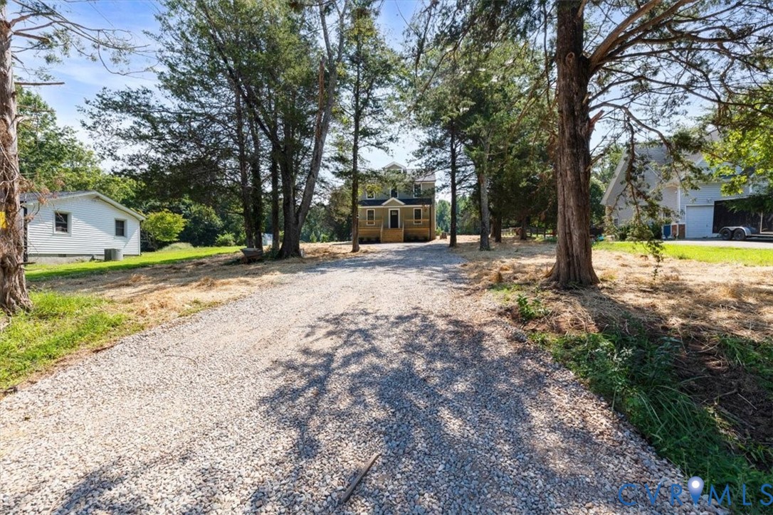Gravel driveway approach leading to a two-story residence with a covered front porch and mature tree-lined grounds