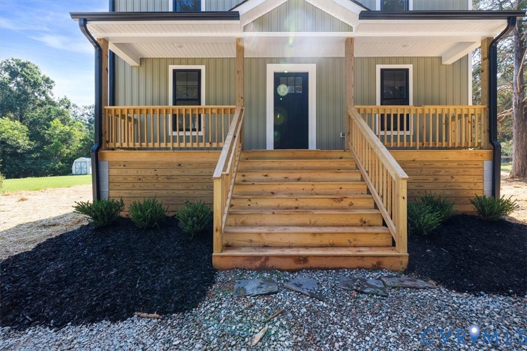 Exterior featuring vertical board-and-batten siding, a covered front porch with wood railings, and a solid-color front door
