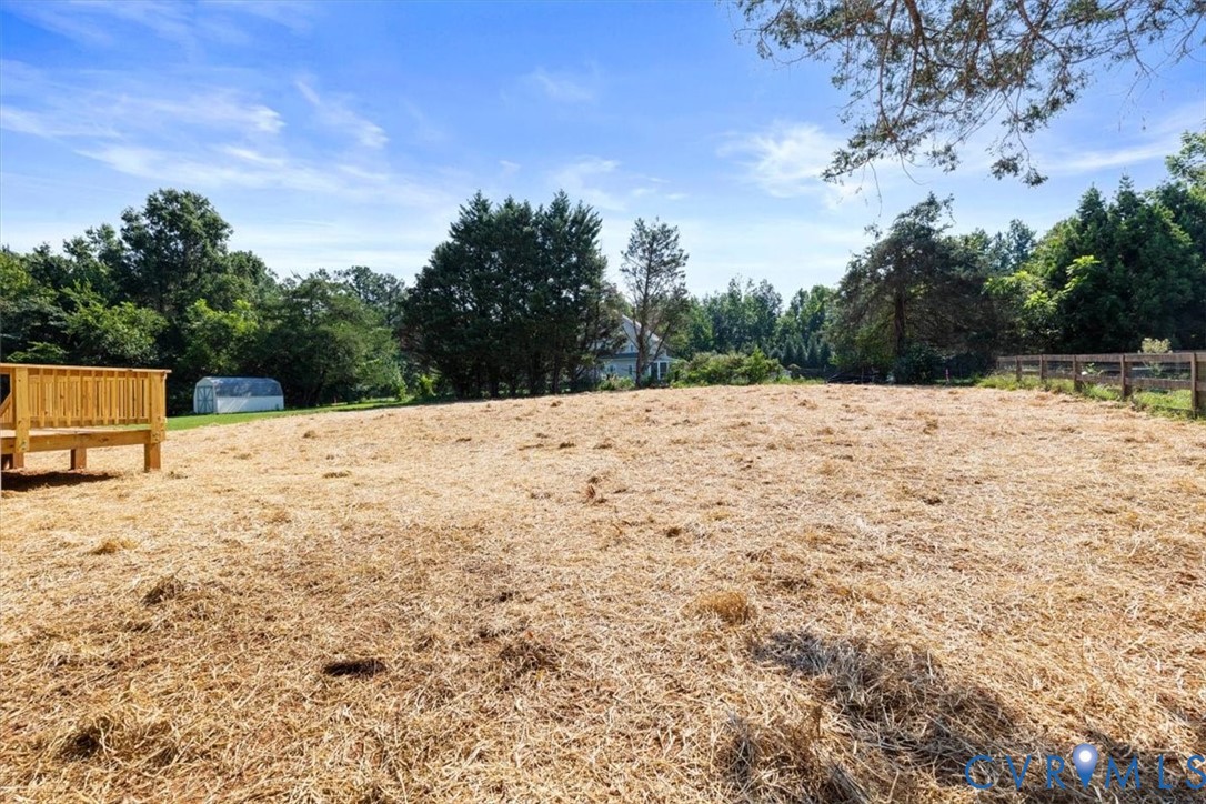 Expansive backyard featuring an elevated wooden deck, post-and-rail wood fencing, and mature perimeter trees
