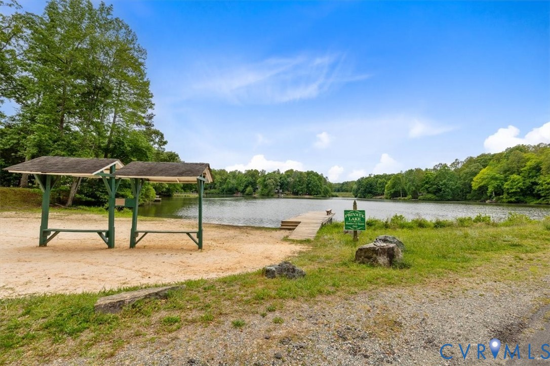 Waterfront property featuring a private lake, a wood-framed dock, and two permanent shaded structures situated on a sandy shoreline