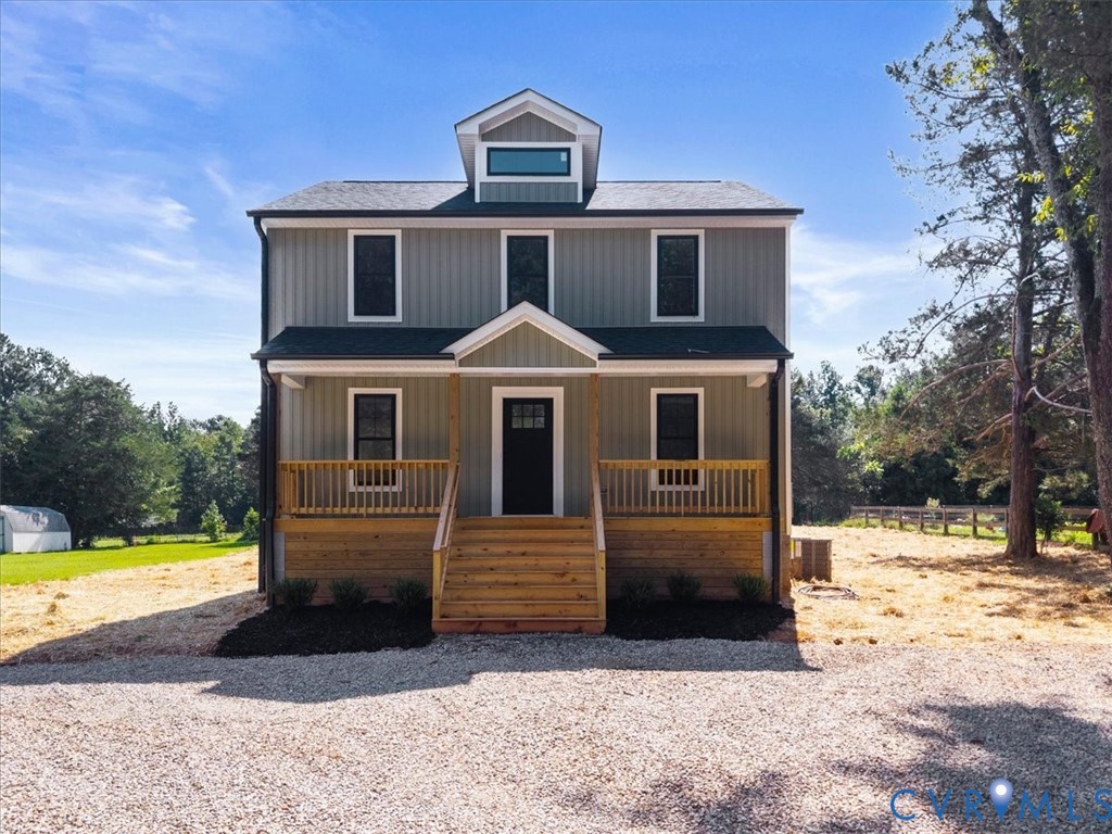 Two-story residence featuring vertical siding, a front porch with natural wood railings, a central dormer window, and a dark shingled roof