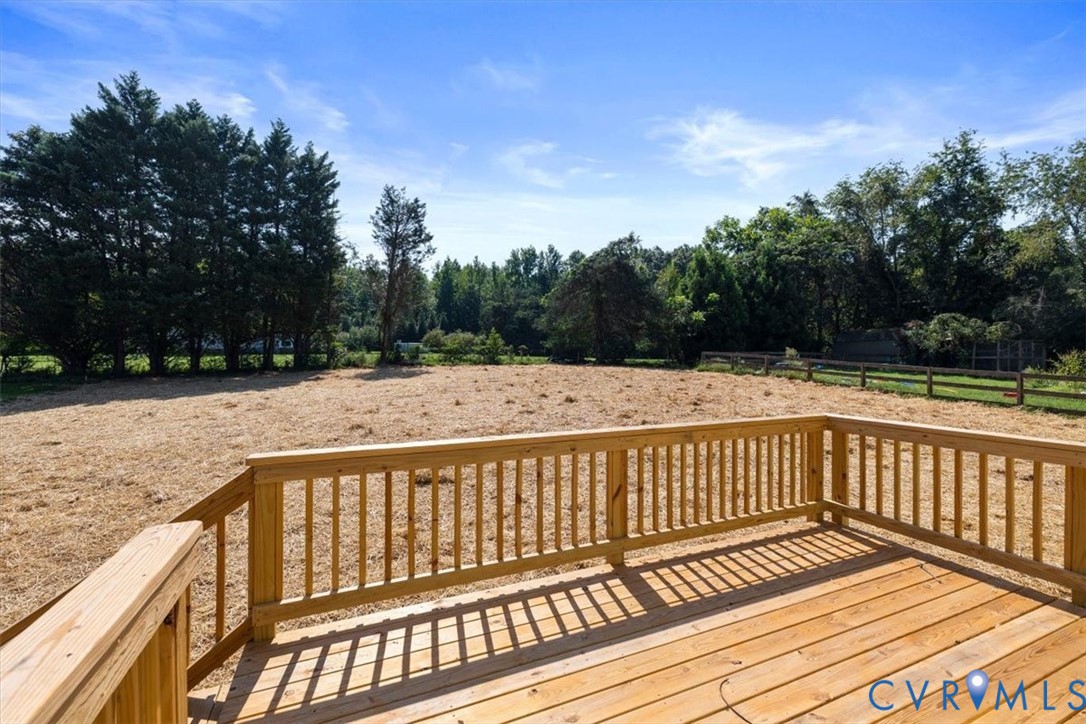 Raised wooden deck featuring vertical baluster railings, open-air lot, and perimeter wood-rail fencing