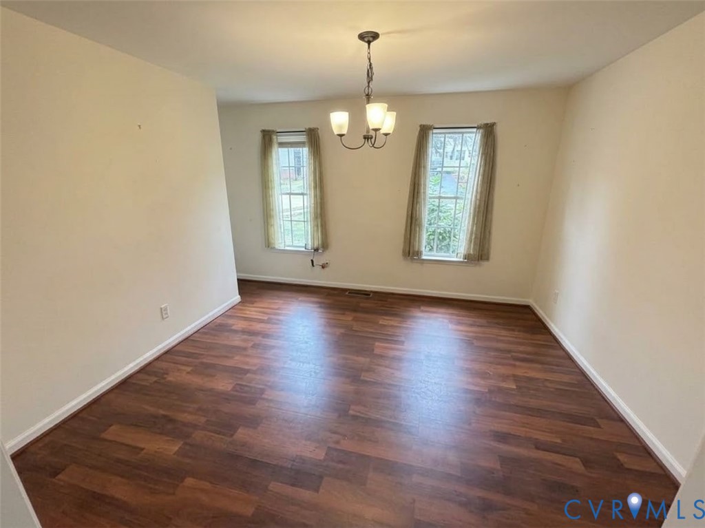 Room featuring wood-finish flooring, two double-hung windows, and a multi-arm chandelier with glass shades