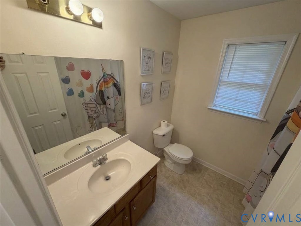 Bathroom featuring a vanity with integrated sink, large wall-mounted mirror, three-light overhead fixture, standard toilet, and window with horizontal blinds