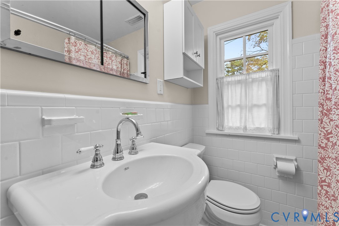 Wall-mounted medicine cabinet with mirror, pedestal sink with polished chrome widespread faucet, and white subway tile wall surround