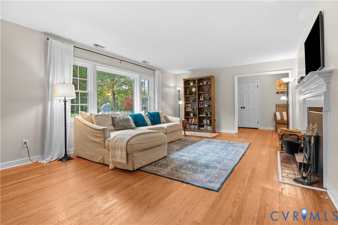 Living area featuring wood-finish flooring, a large picture window, and a fireplace with a traditional mantel and ceramic tile hearth