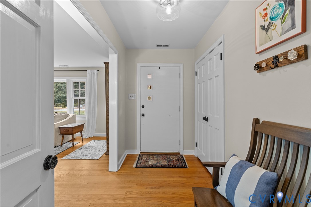 Foyer featuring wood-finish flooring, a six-panel entry door, a double-door coat closet, and a ceiling-mounted glass globe fixture