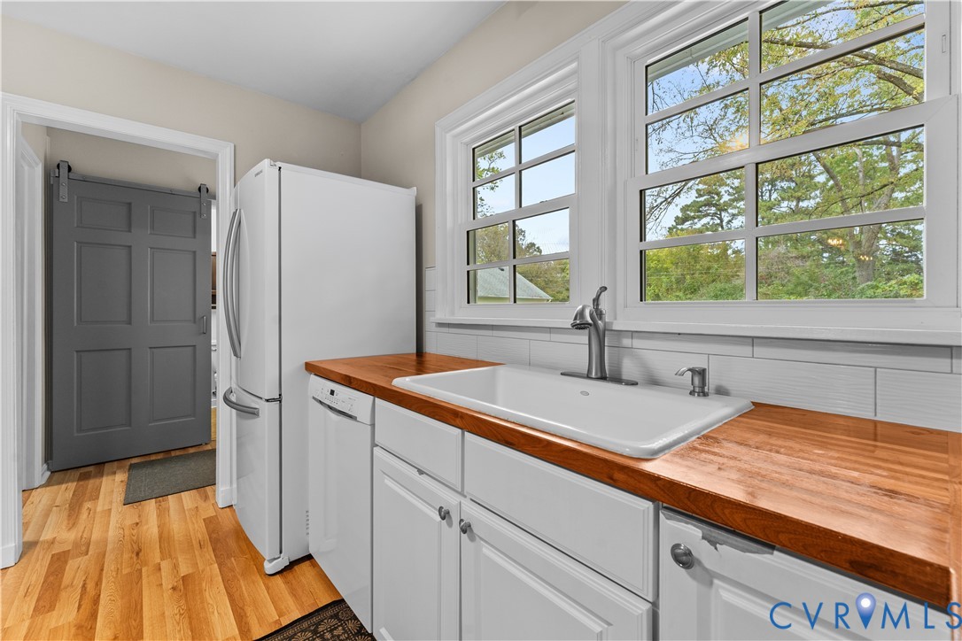 Kitchen featuring white cabinetry, wood countertops, a farmhouse-style apron sink, white tile backsplash, and a gray sliding barn door