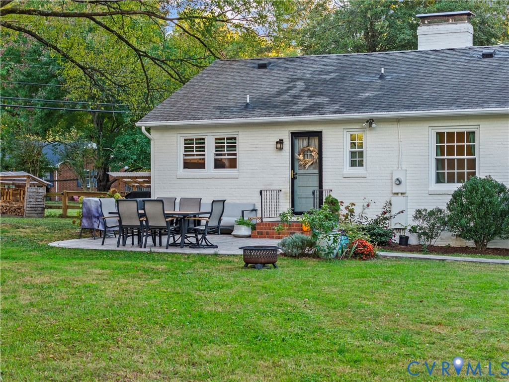 White painted brick exterior featuring a rear stone paver patio, a brick chimney, and multi-light windows