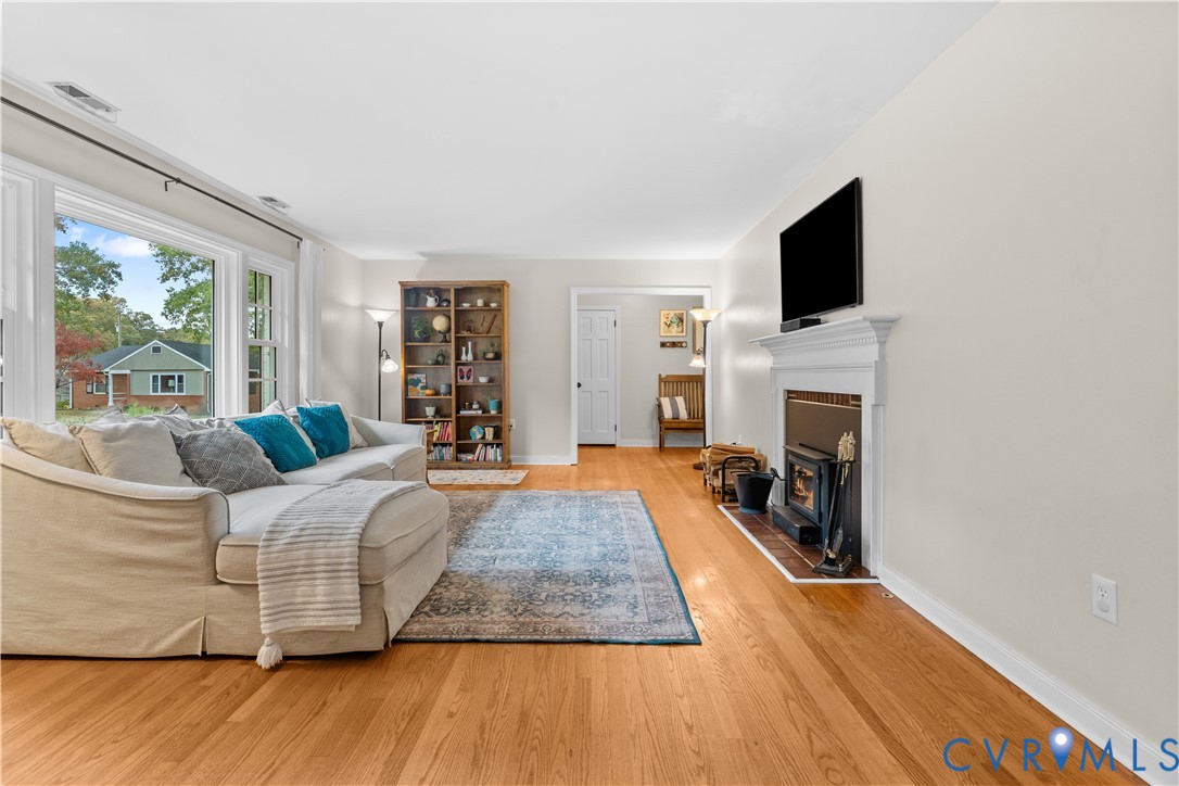 Living area featuring wood-finish flooring, a wood-burning fireplace with a white mantel, and large picture windows