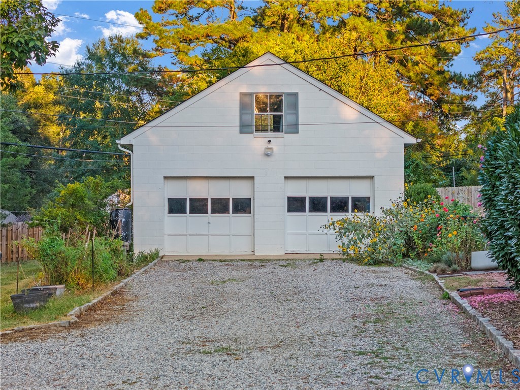 Detached two-car garage featuring white block exterior, dual panelled overhead doors, and an upper-level window with shutters