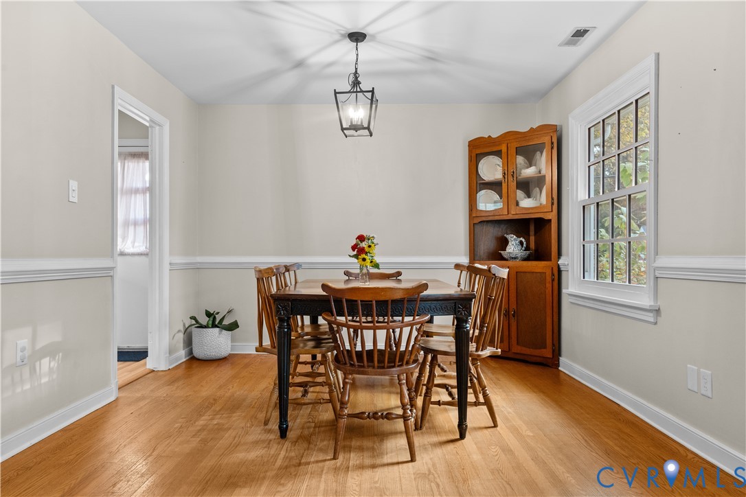 Dining area featuring wood-finish flooring, white chair rail molding, a built-in wooden corner hutch, and a hanging geometric lantern pendant light