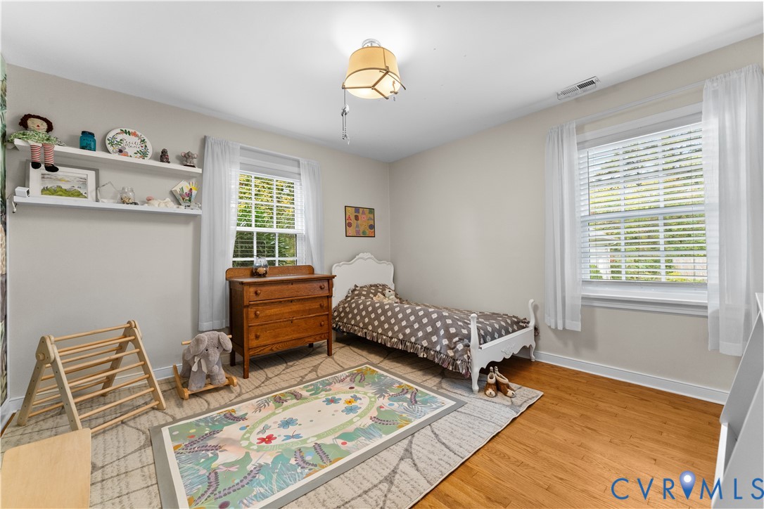 Bedroom featuring wood-finish flooring, dual windows with blinds, and built-in wall shelving
