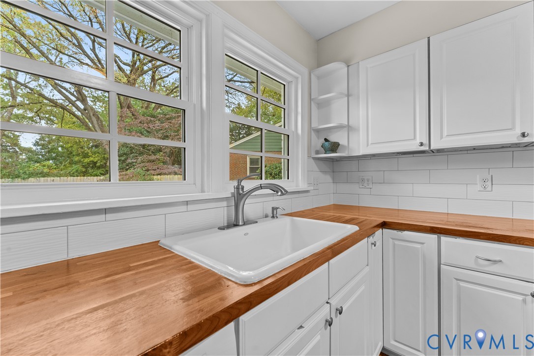 Kitchen featuring butcher block countertops, white shaker-style cabinetry, a white apron-front sink with a high-arch faucet, and white subway tile backsplash