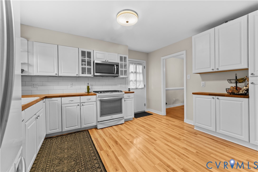Kitchen featuring white shaker-style cabinetry, wood-finish countertops, subway tile backsplash, and light-tone wood-finish flooring