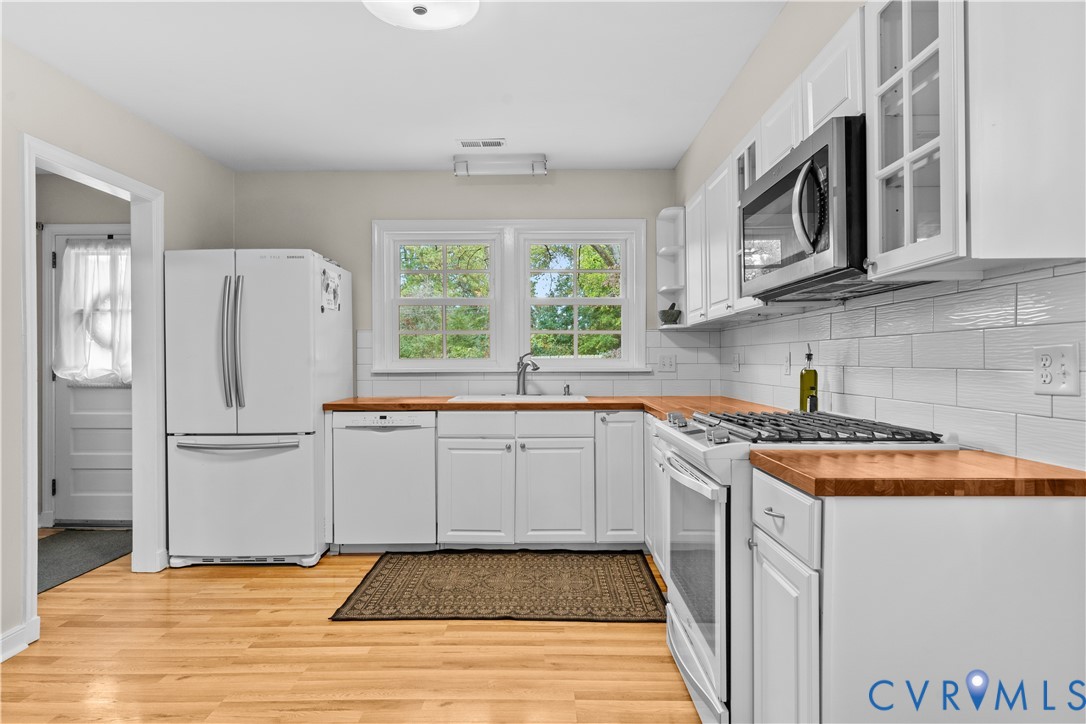 Kitchen featuring white shaker-style cabinetry, wood-finish countertops, subway tile backsplash, stainless steel microwave, and wood-finish flooring