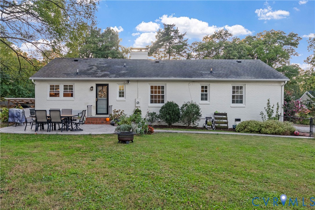 Painted brick exterior featuring a multi-paned window configuration, rear brick stoop, and expansive lawn with mature perimeter trees