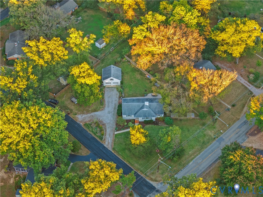 Aerial perspective of a detached residential property featuring a sprawling lot, a detached garage, a gravel driveway, and mature deciduous trees Aerial perspective of a detached residential property featuring a sprawling lot, a detached garage, a gravel driveway, and mature deciduous trees