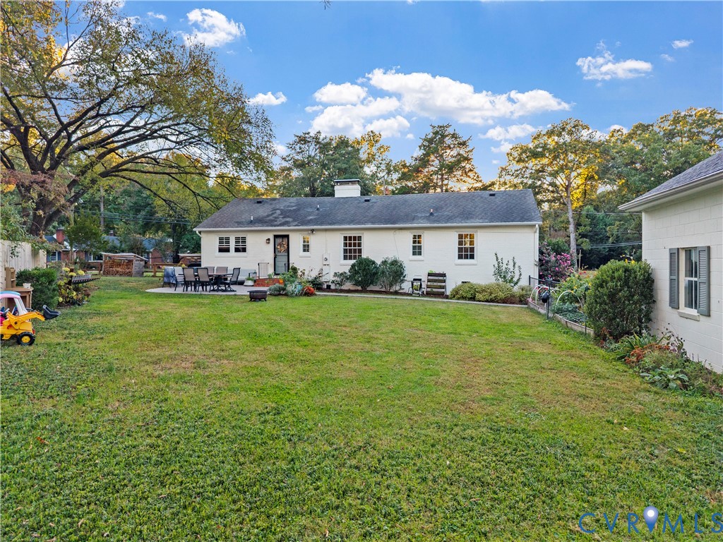Spacious backyard featuring a manicured lawn, paved patio area, white brick exterior, and mature trees