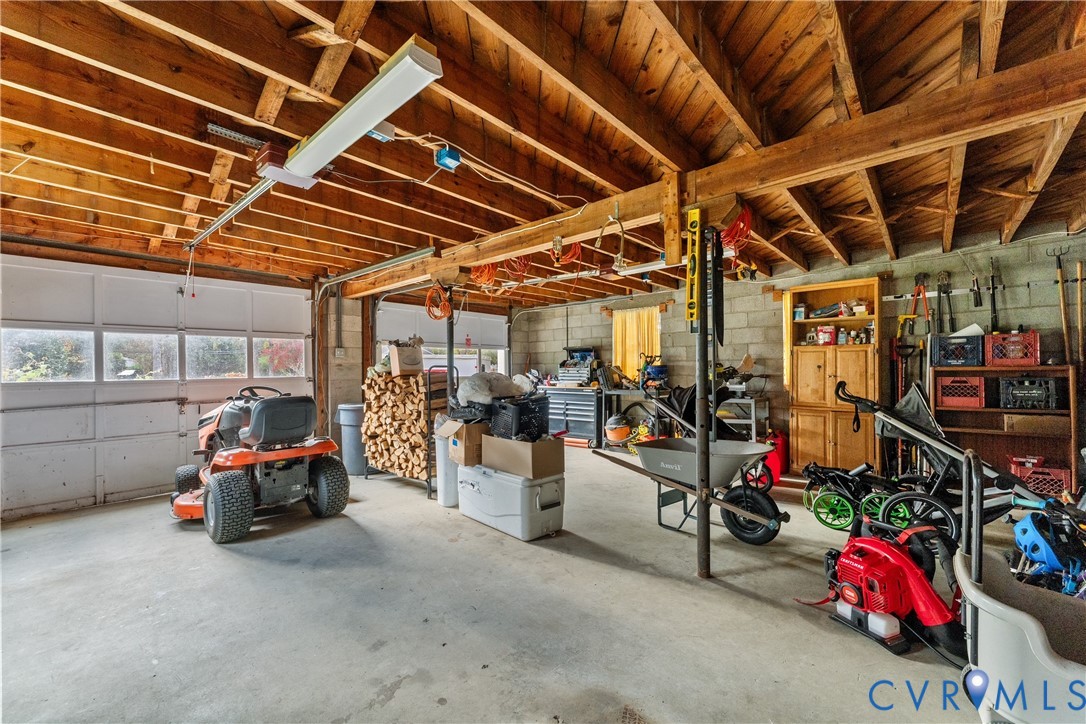 Garage featuring exposed wooden rafters, concrete flooring, concrete masonry unit walls, built-in wooden shelving, and a paneled garage door